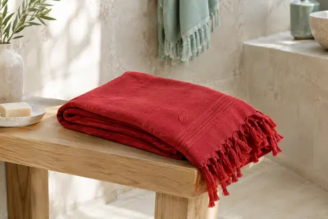 Fouta en coton rouge pliée sur un banc en bois clair dans une salle de bain lumineuse