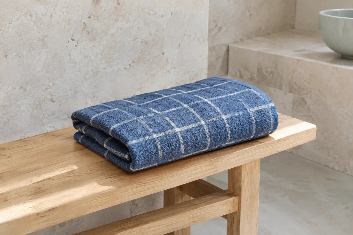 Serviette de hammam en coton bleu à carreaux, pliée sur un banc en bois clair