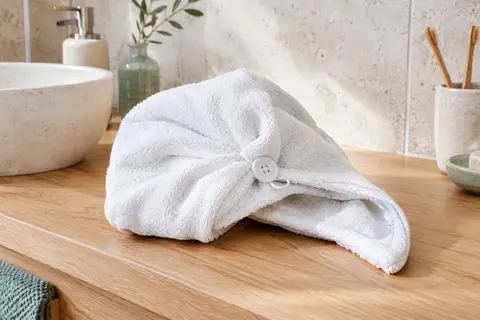 Turban à cheveux blanc en coton, avec bouton et boucle, posé sur un meuble de salle de bain en bois clair.