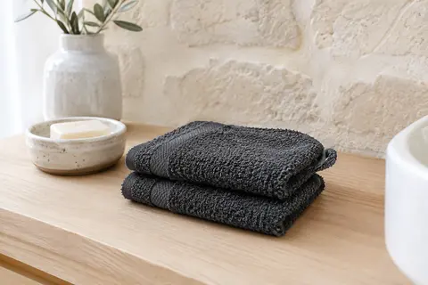 Deux gants de toilette anthracite en coton éponge pliés sur une tablette en bois clair