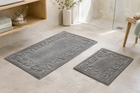 Deux tapis de bain gris au motif grec, posés sur un sol clair dans une salle de bain lumineuse.