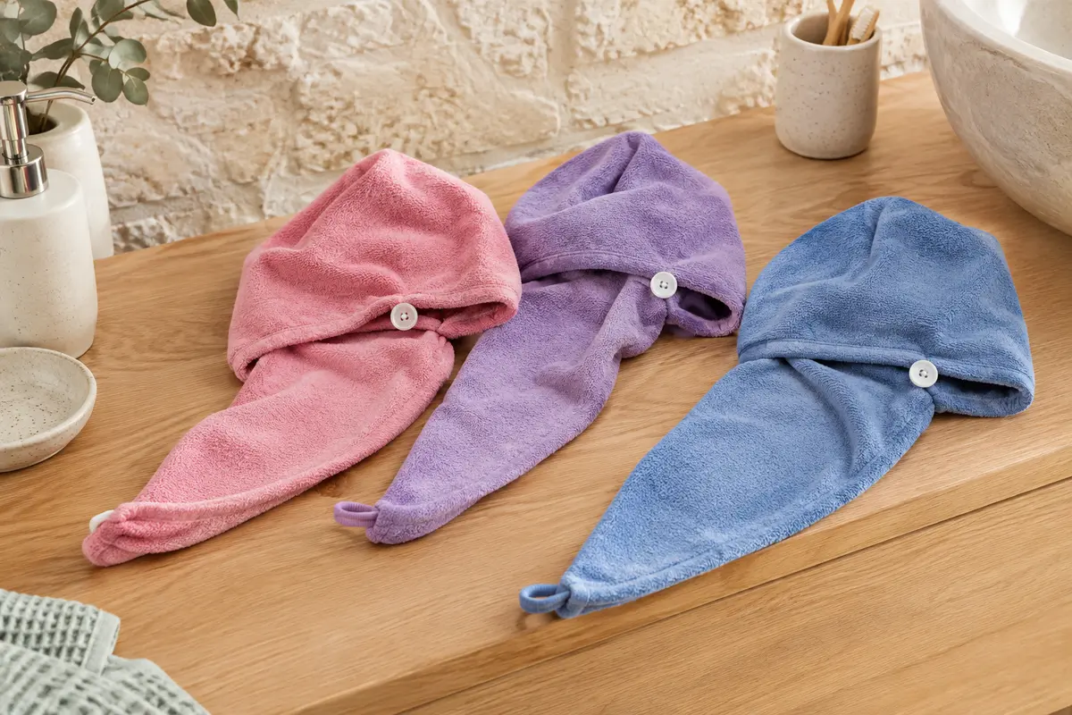 Trois turbans cheveux en microfibre rose, violet et bleu présentés dans une salle de bain lumineuse