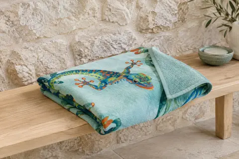 Serviette de plage en coton au motif imprimé Gecko, pliée sur un banc en bois blond