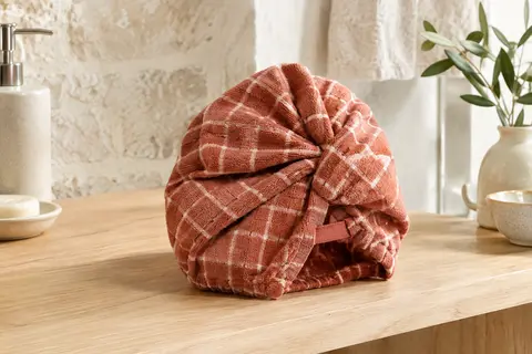 Serviette cheveux en microfibre à carreaux terre cuite, pliée sur une tablette en bois blond dans une salle de bain lumineuse.