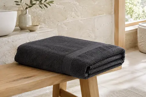 Drap de bain anthracite en coton éponge plié dans une salle de bain claire