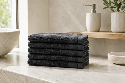 Lot de cinq serviettes invité en coton éponge anthracite pliées sur une étagère de salle de bain