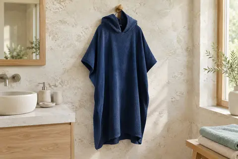 Poncho de bain adulte bleu foncé en microfibre suspendu dans une salle de bain lumineuse.