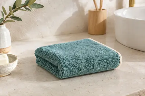 Serviette invité Möve Superwuschel en coton épais, pliée sur une pierre claire dans une salle de bain lumineuse