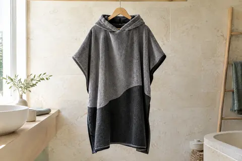Poncho de surf gris et noir en velours de coton, suspendu dans une salle de bain lumineuse.