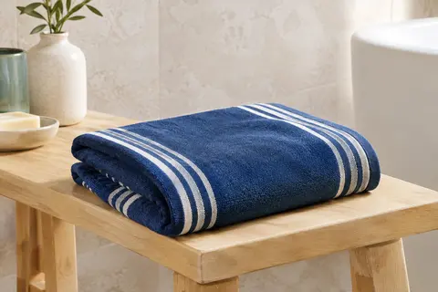 Serviette de plage microfibre bleu profond à rayures, pliée sur un banc en bois clair