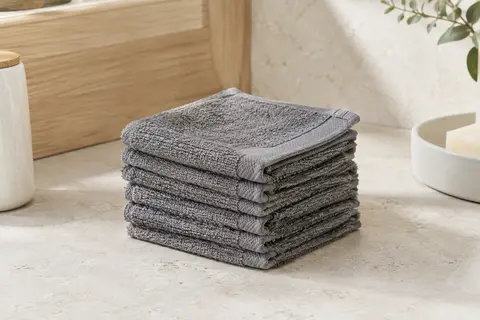 Pile de gants de toilette gris en coton, pliés sur une surface de pierre claire dans une salle de bain lumineuse