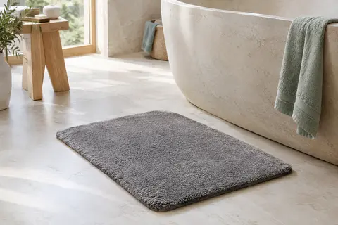 Tapis de bain rectangulaire gris en microfibre épaisse posé sur un sol clair de salle de bain