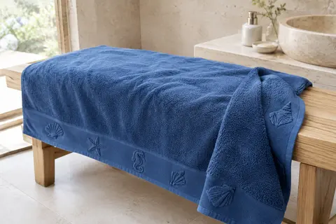 Serviette de plage bleue en coton, motifs marins tissés et faces velours et éponge, dans une salle de bain claire.